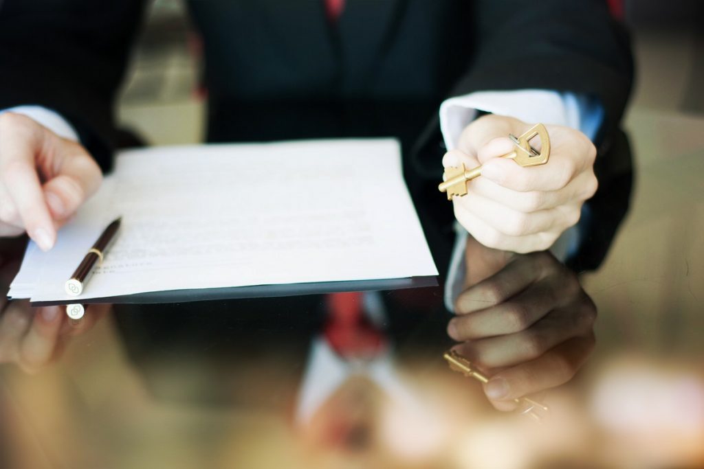 Person holding house keys and a contract