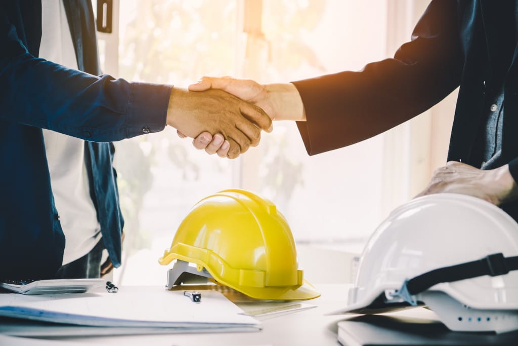 Two men shaking hands near a table with hard hats and papers
