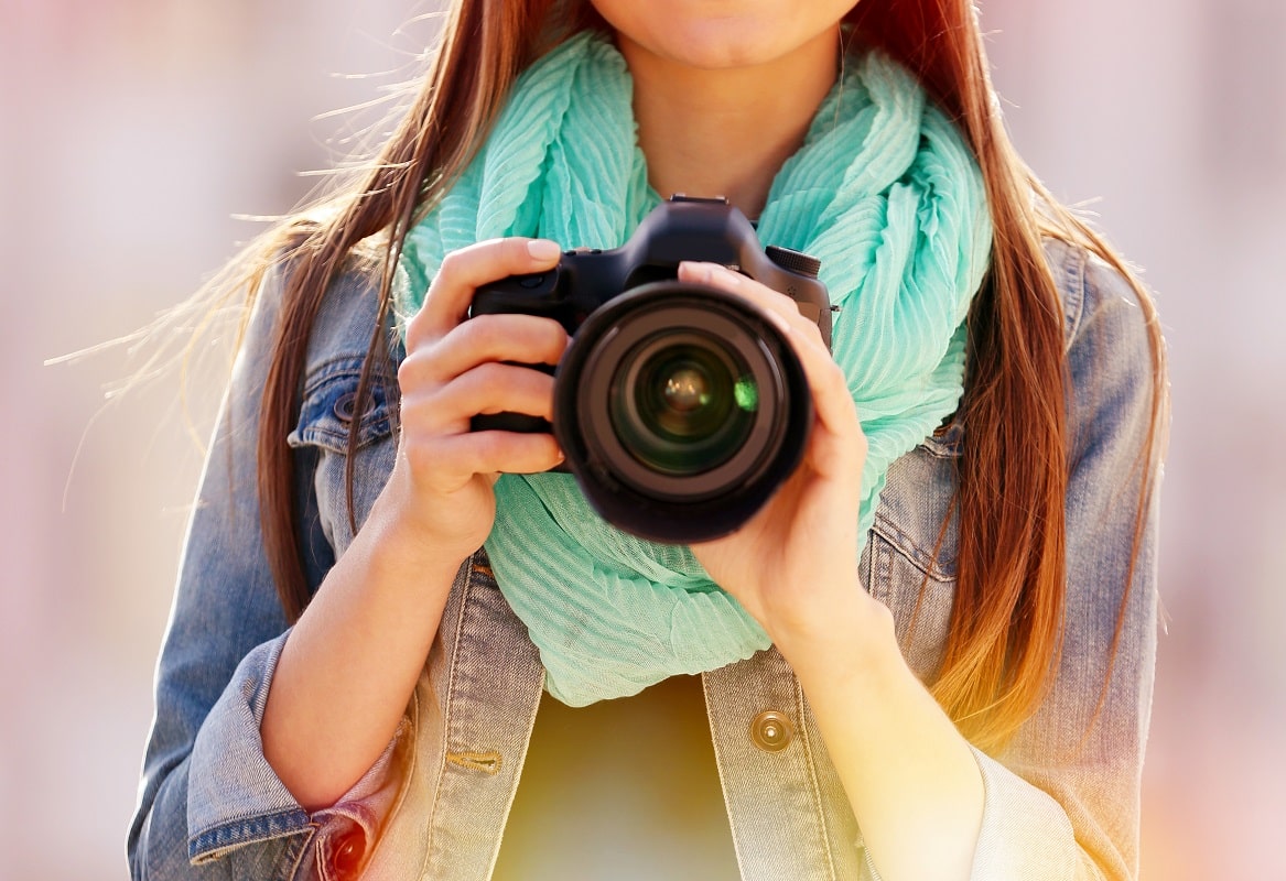 Young woman holding a camera while standing outdoors.